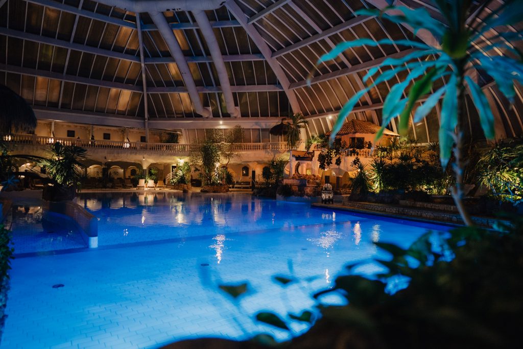 Innenpool der Medi Therme Bochum unter großer Glaskuppel mit tropischen Pflanzen und Beleuchtung